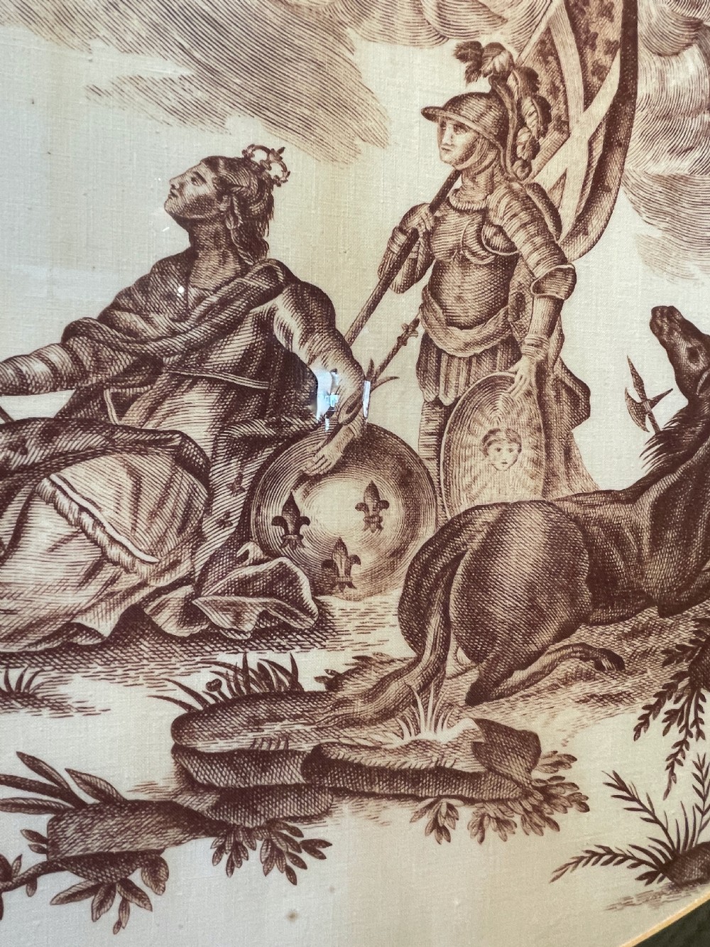 An oval copperplate-printed sepia textile fragment depicting an allegorical scene set inside a green mount and dark wooden frame. View IV