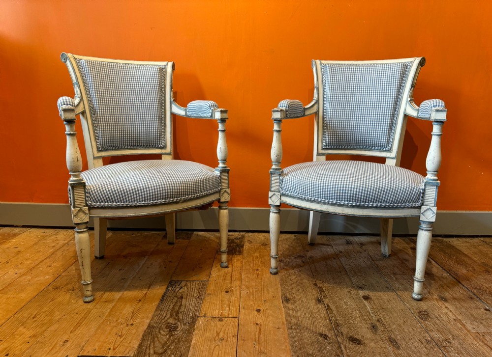 Pair of vintage French armchairs featuring off-white distressed painted frames, fluted turned front legs, and blue and white checked fabric upholstery.