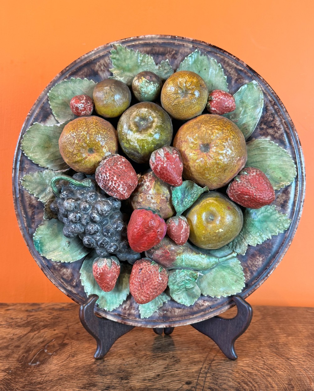 A circular 19th-century Portuguese majolica earthenware dish featuring high-relief ceramic fruit including grapes, strawberries, and oranges surrounded by green leaves.