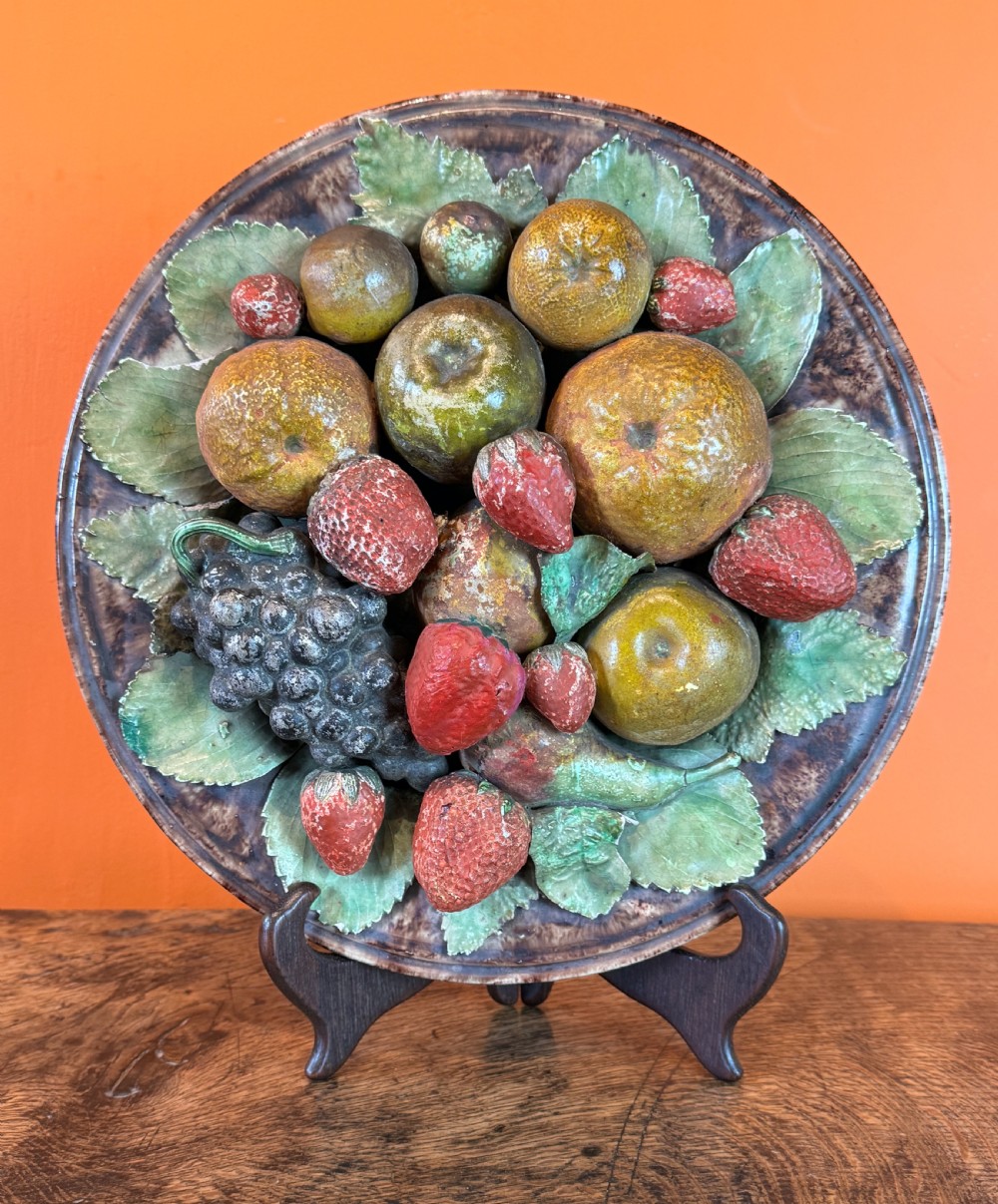 A circular 19th-century Portuguese majolica earthenware dish featuring high-relief ceramic fruit including grapes, strawberries, and oranges surrounded by green leaves. View II