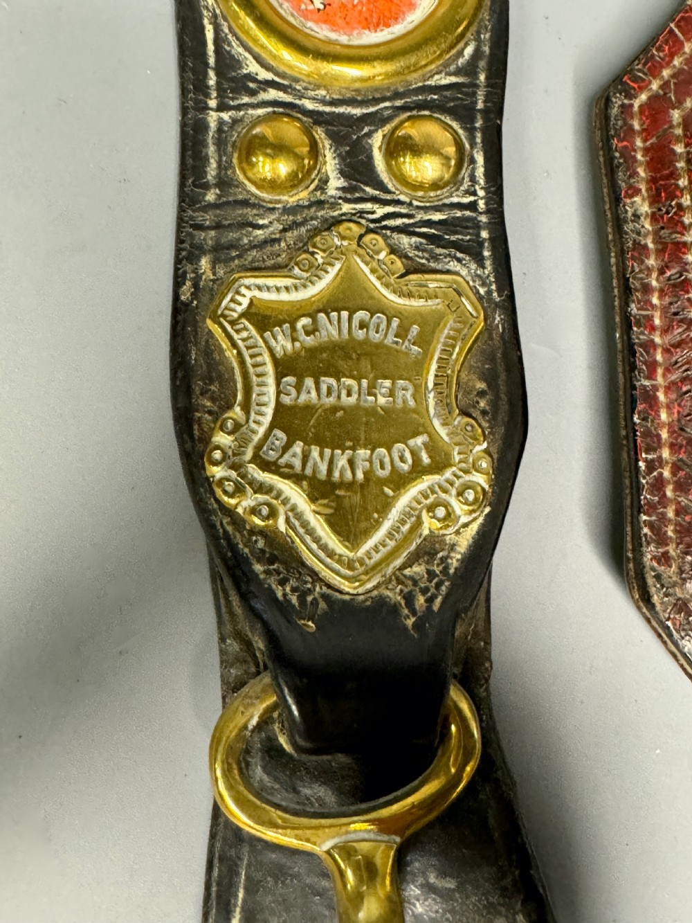 Two vertical Victorian leather martingales featuring polished cast brass amulets, stamped maker shields, and brass hooks against a neutral background. View III