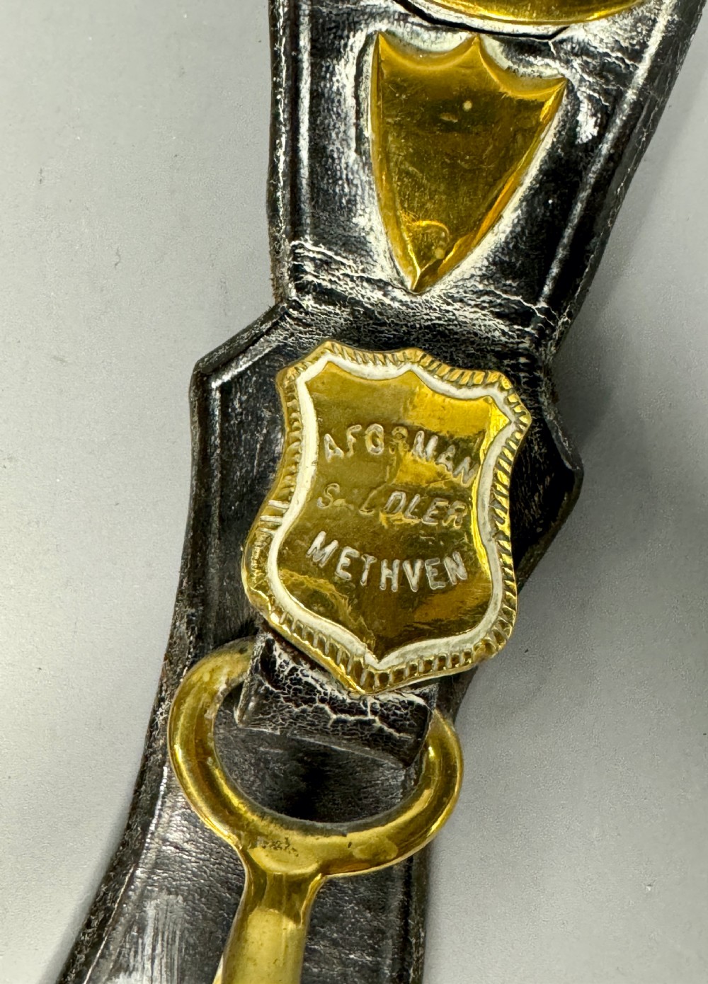Two vertical Victorian leather martingales featuring polished cast brass amulets, stamped maker shields, and brass hooks against a neutral background. View IV