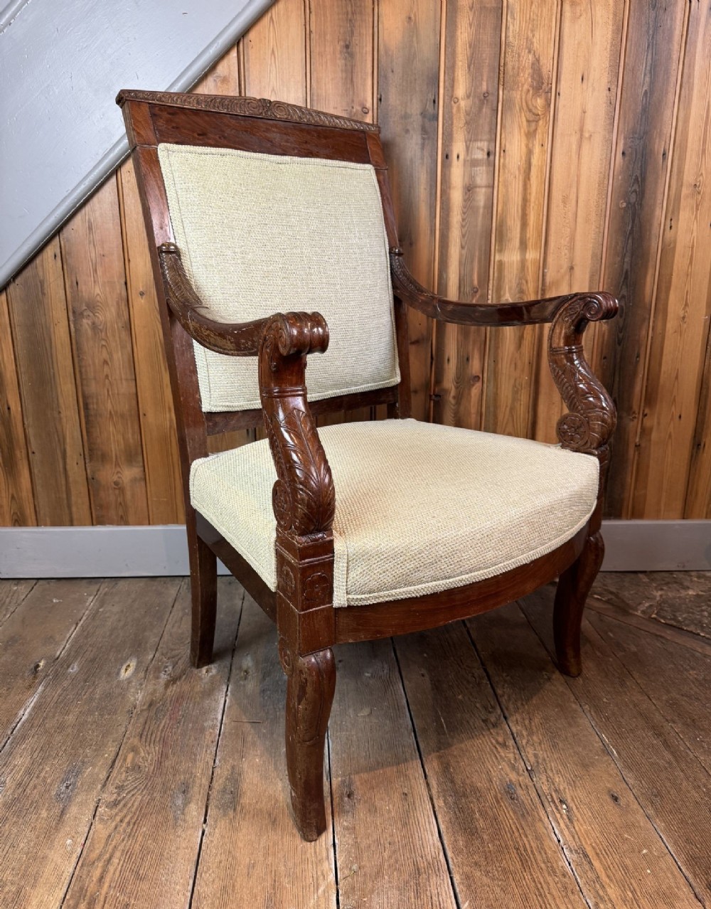 An antique French Empire revival open armchair crafted from dark mahogany wood with neutral upholstered panels on the backrest and seat.