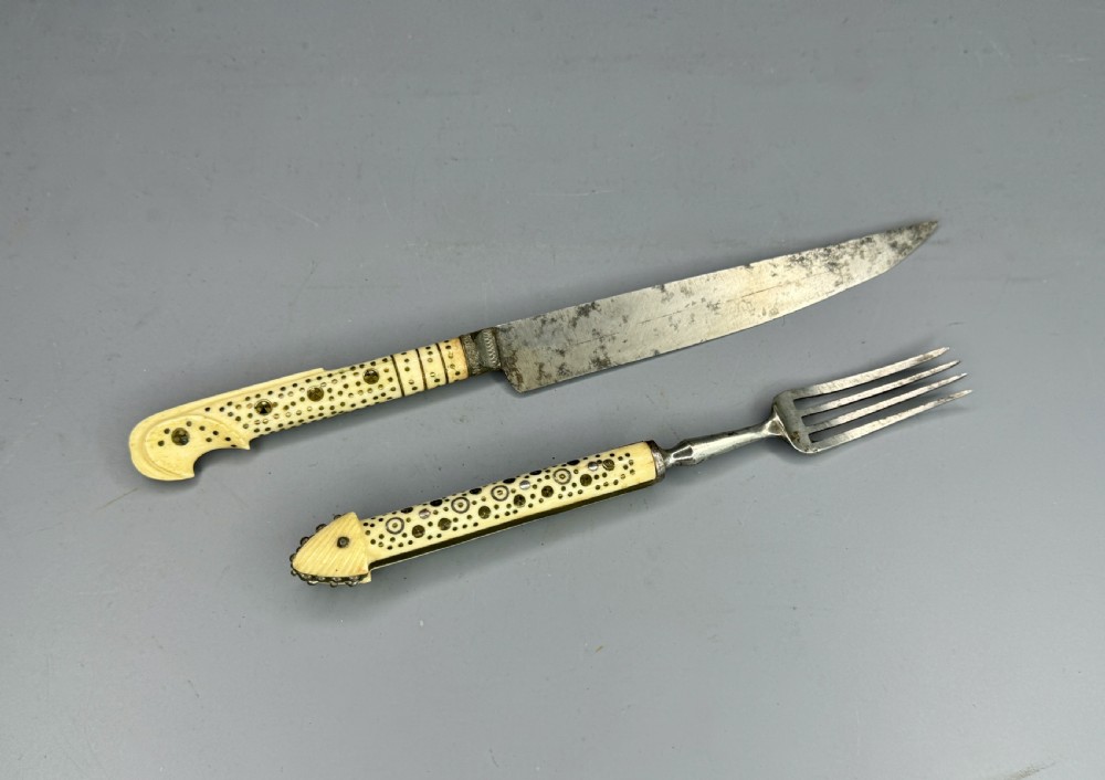 A 19th-century Balkan knife and fork set featuring carved cream bone handles with inlaid circular geometric designs and steel working ends.