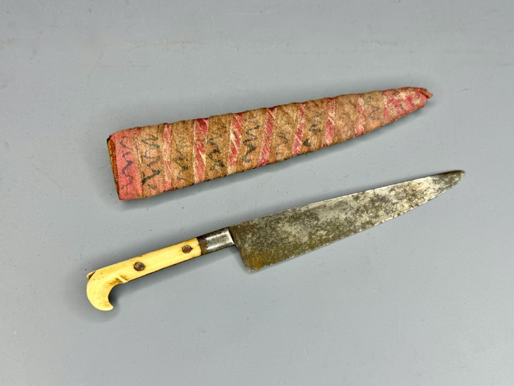 A 19th-century Balkan dagger featuring a single-edged steel blade, a carved cream bone handle with metal rivets, and a patterned fabric sheath.