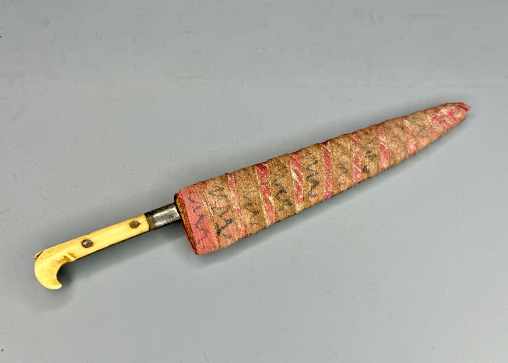 A 19th-century Balkan dagger featuring a single-edged steel blade, a carved cream bone handle with metal rivets, and a patterned fabric sheath. View II