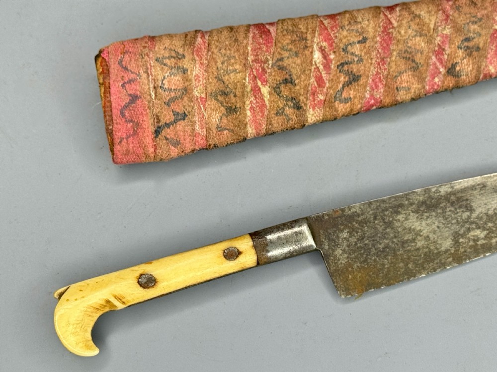 A 19th-century Balkan dagger featuring a single-edged steel blade, a carved cream bone handle with metal rivets, and a patterned fabric sheath. View III