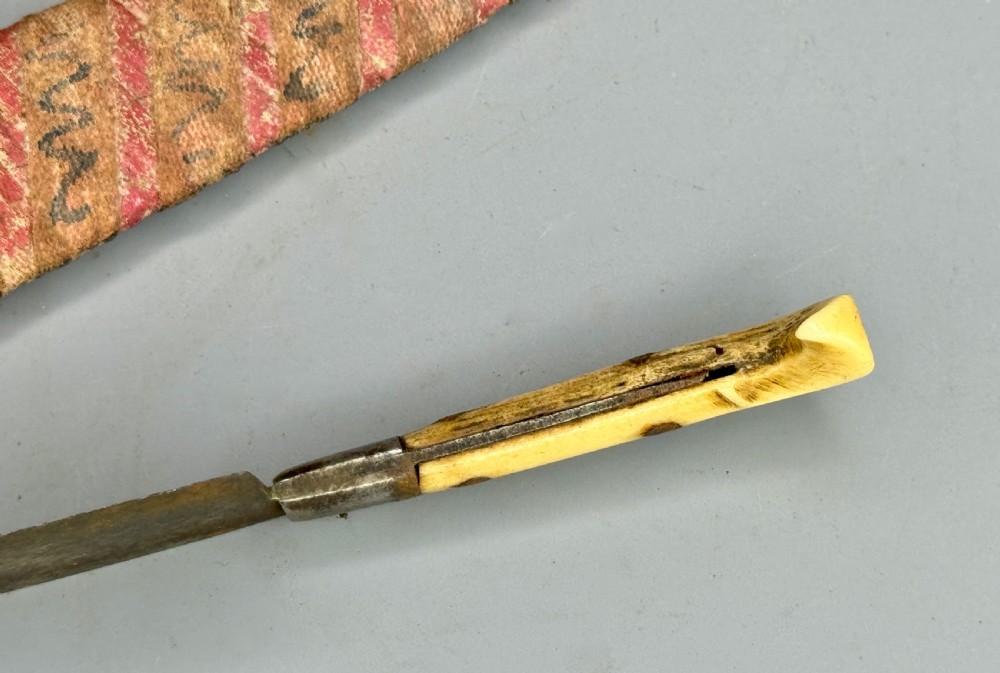 A 19th-century Balkan dagger featuring a single-edged steel blade, a carved cream bone handle with metal rivets, and a patterned fabric sheath. View IV