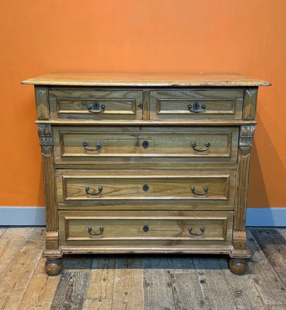 An antique pine chest of drawers featuring two upper small drawers over three full-width drawers with carved side pilasters and brass handles.