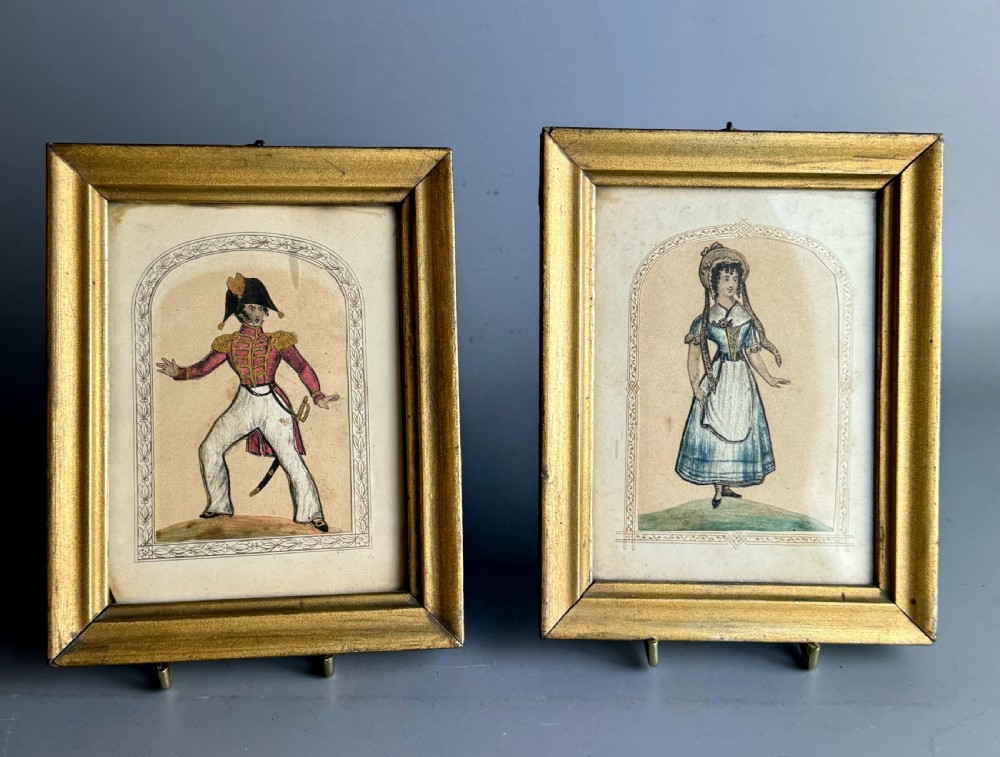 A pair of framed mid-nineteenth-century theatrical silkwork pictures depicting figures in period costume within moulded gilt wooden frames.