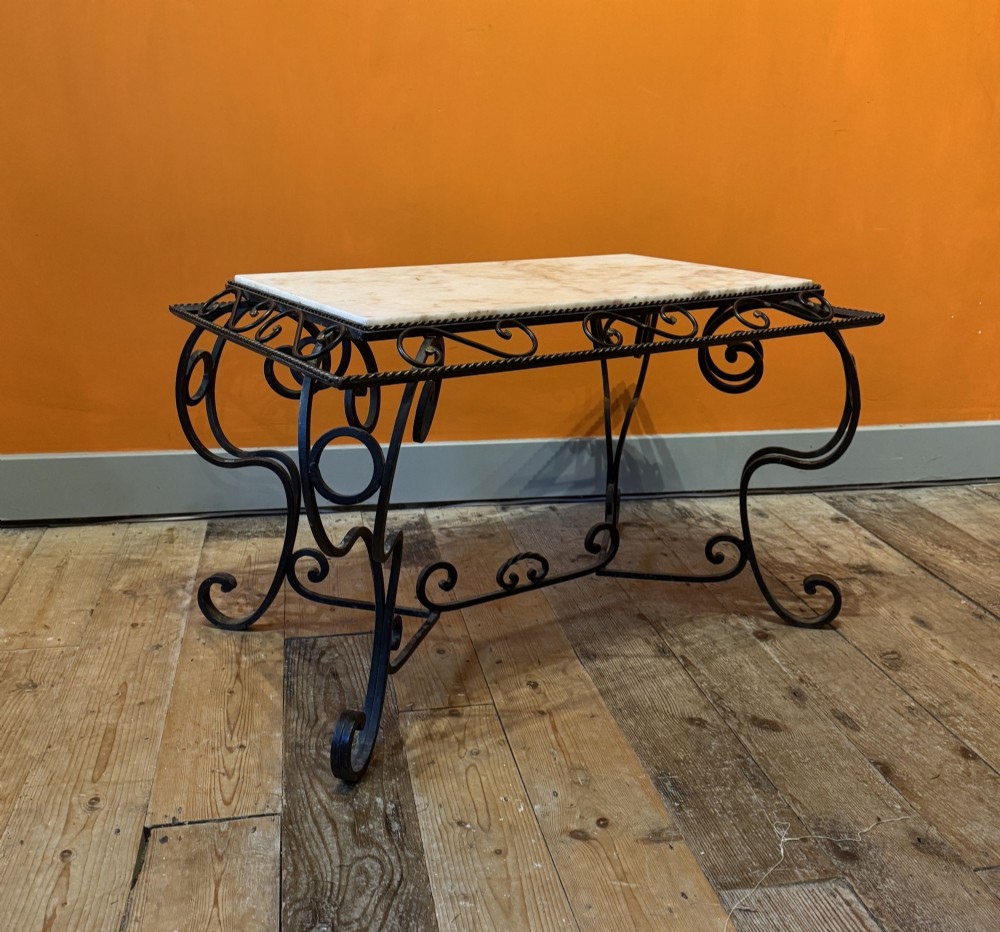 A rectangular French coffee table with a pale marble top set upon a black wrought iron base featuring decorative scrollwork.