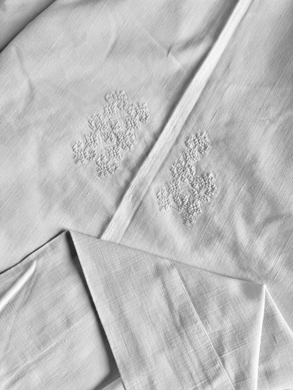 Close-up view of a white handwoven homespun linen sheet featuring white hand-embroidered monograms along a central seam.