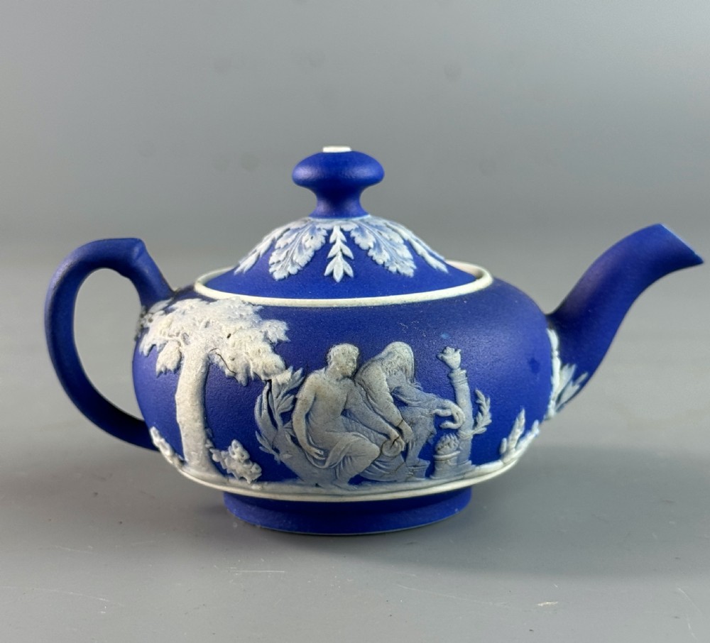 A miniature blue stoneware teapot featuring white classical relief figures and a leaf motif on the lid. View III