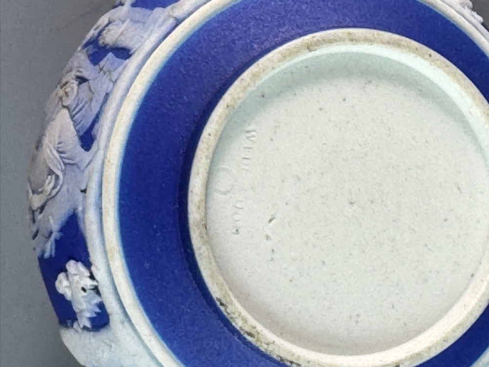 A miniature blue stoneware teapot featuring white classical relief figures and a leaf motif on the lid. View VI