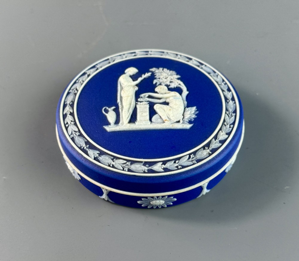 A circular royal blue jasperware patch box featuring white neoclassical relief figures on the lid and floral sprigging around the rim.
