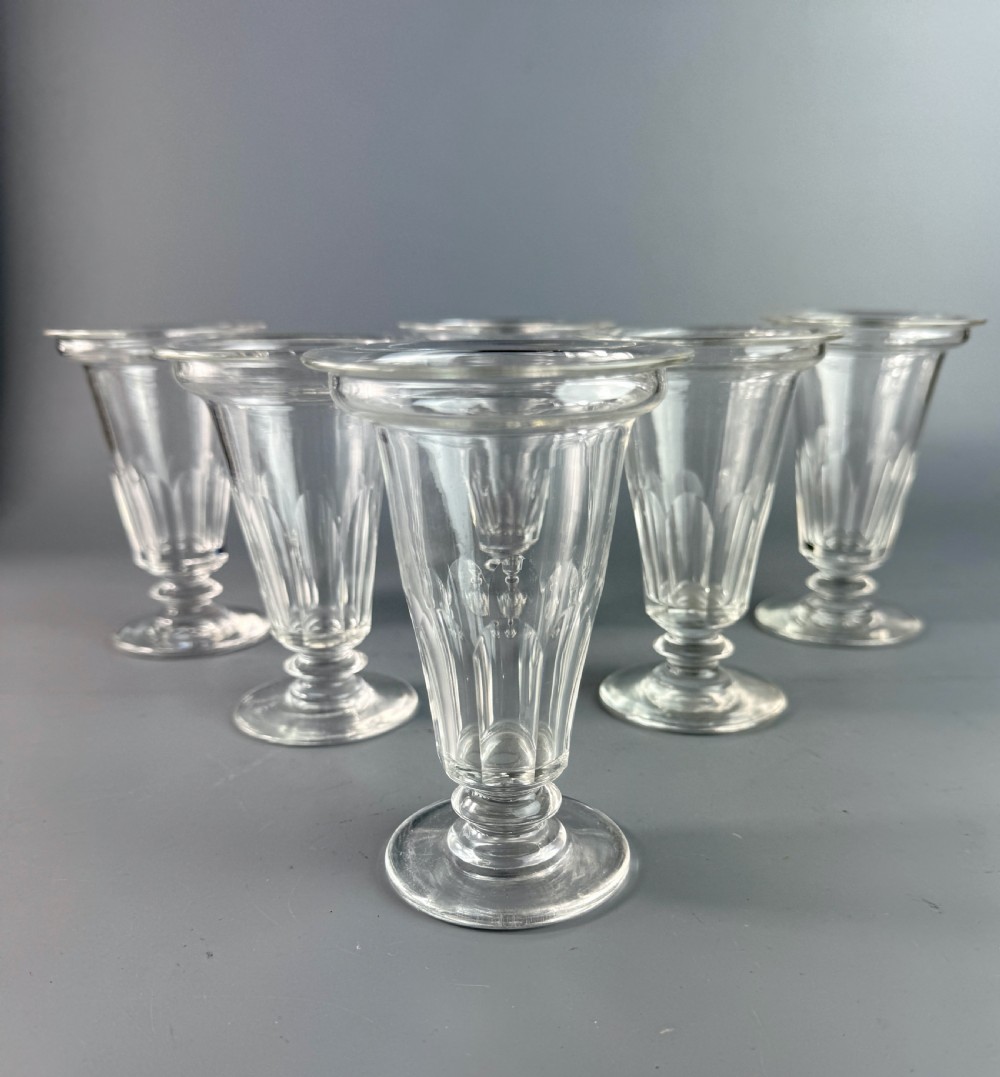 A set of six clear Georgian glass jelly cups featuring fluted tapered bowls, dish tops, knopped stems, and circular bases.