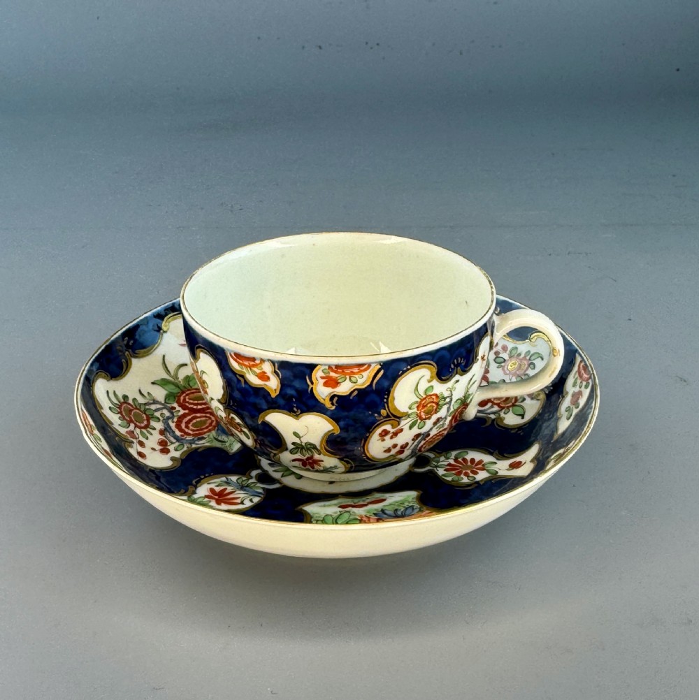 An eighteenth-century Worcester soft-paste porcelain teacup and saucer decorated with a blue scale ground and hand-painted floral cartouches.