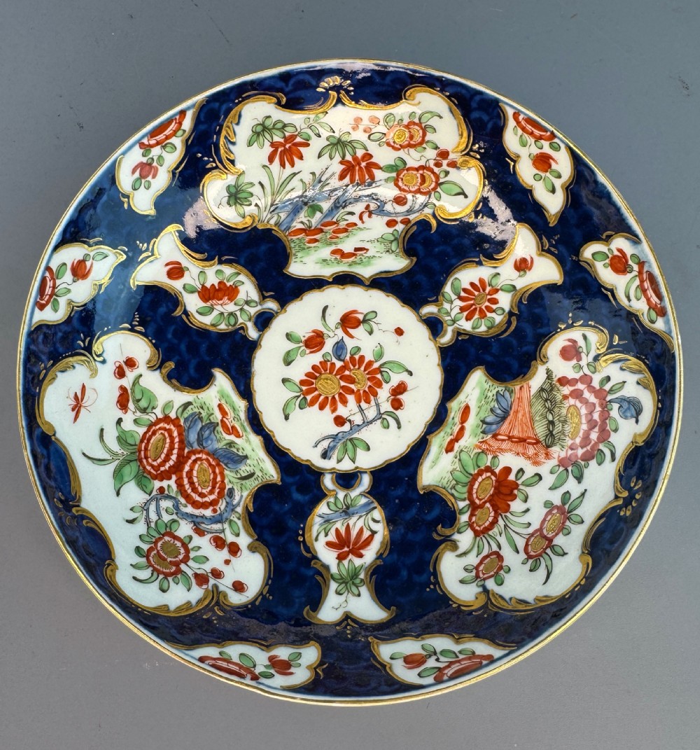 An eighteenth-century Worcester soft-paste porcelain teacup and saucer decorated with a blue scale ground and hand-painted floral cartouches. View II