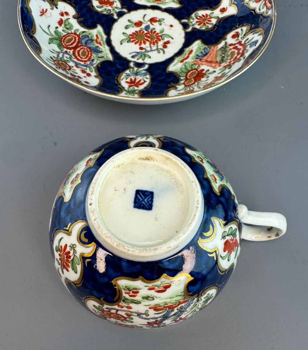 An eighteenth-century Worcester soft-paste porcelain teacup and saucer decorated with a blue scale ground and hand-painted floral cartouches. View III