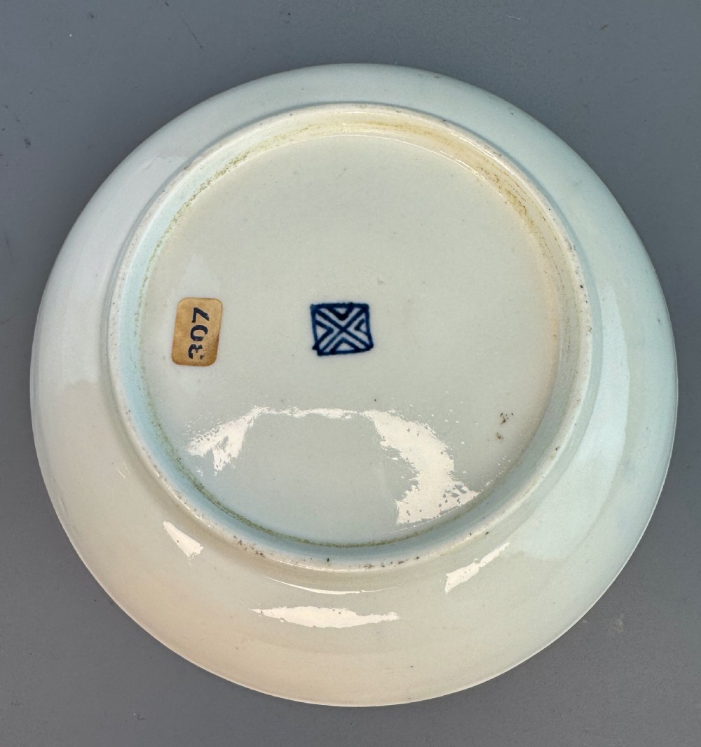 An eighteenth-century Worcester soft-paste porcelain teacup and saucer decorated with a blue scale ground and hand-painted floral cartouches. View V