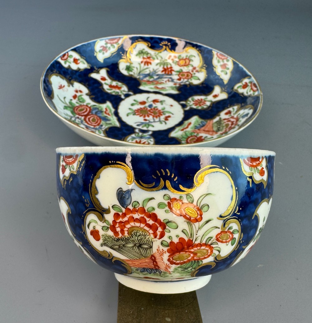 An eighteenth-century Worcester soft-paste porcelain teacup and saucer decorated with a blue scale ground and hand-painted floral cartouches. View VII