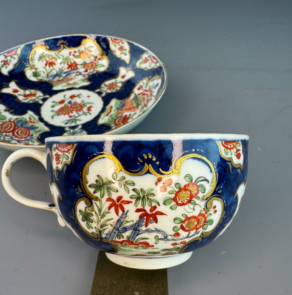 An eighteenth-century Worcester soft-paste porcelain teacup and saucer decorated with a blue scale ground and hand-painted floral cartouches. View VIII