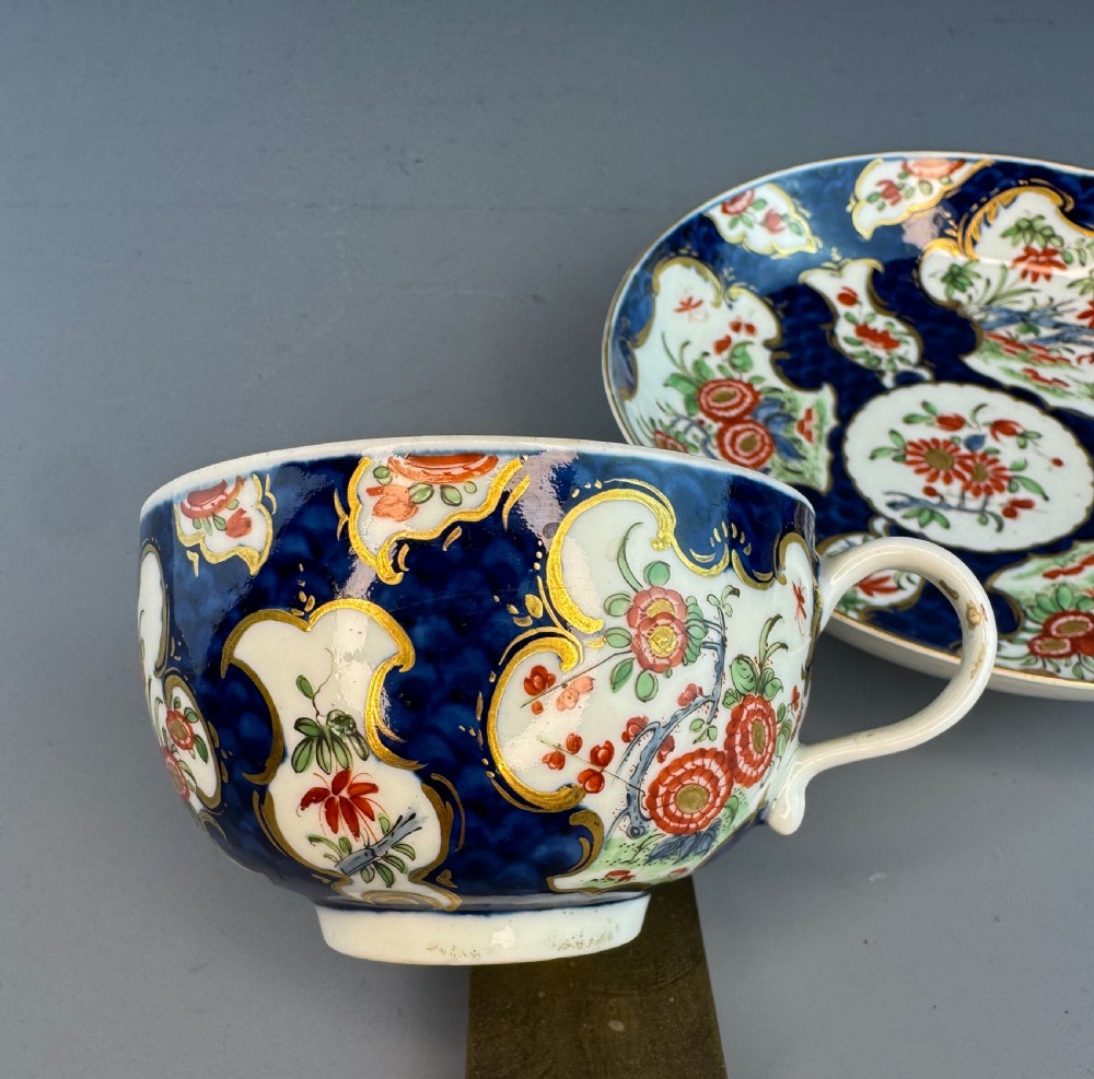 An eighteenth-century Worcester soft-paste porcelain teacup and saucer decorated with a blue scale ground and hand-painted floral cartouches. View IX