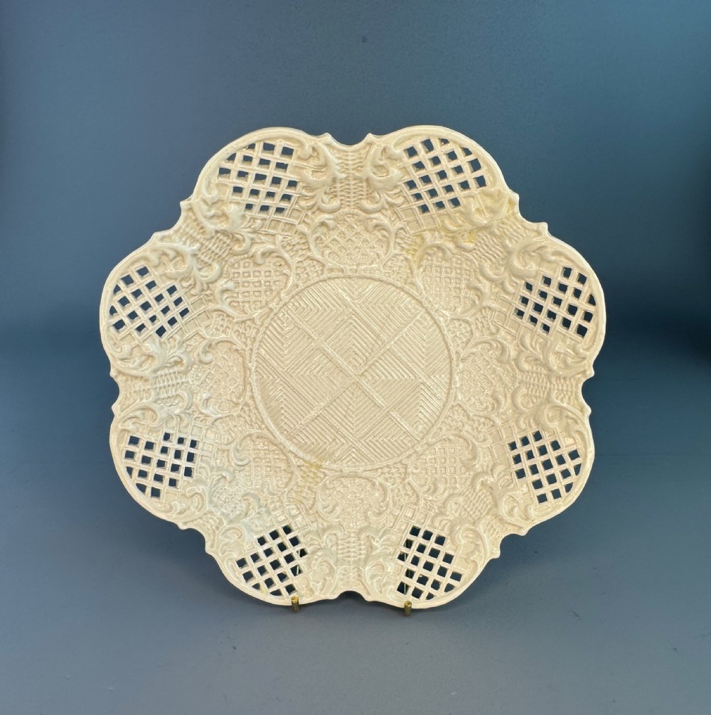 An 18th-century cream-coloured Staffordshire saltglaze stoneware lobed plate featuring lattice piercing and relief-moulded scrollwork details.
