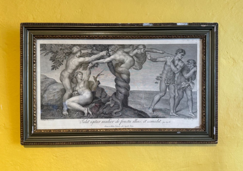 A framed monochrome copperplate engraving depicting the Temptation and Expulsion of Adam and Eve after Michelangelo, encased within a dark moulded frame with a Latin text inscription below.