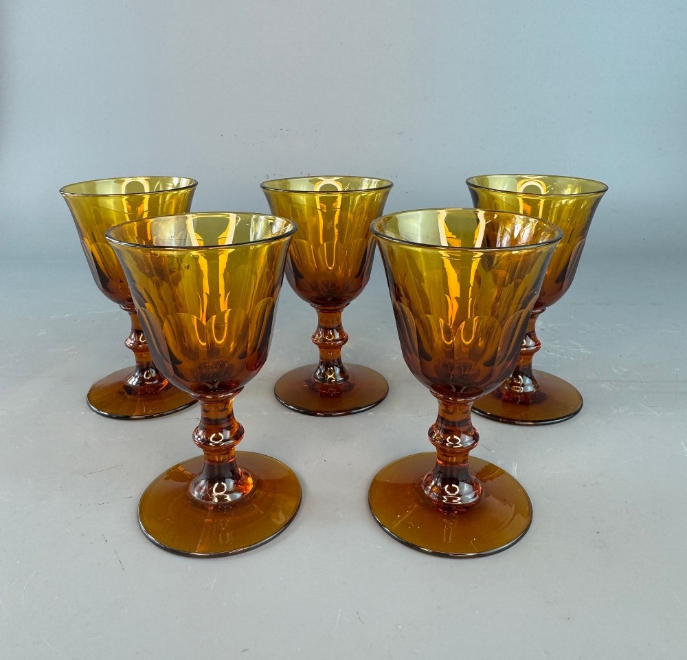 A set of five Victorian amber-coloured cut glass port glasses with flared bowls, faceted bases, and knopped stems.