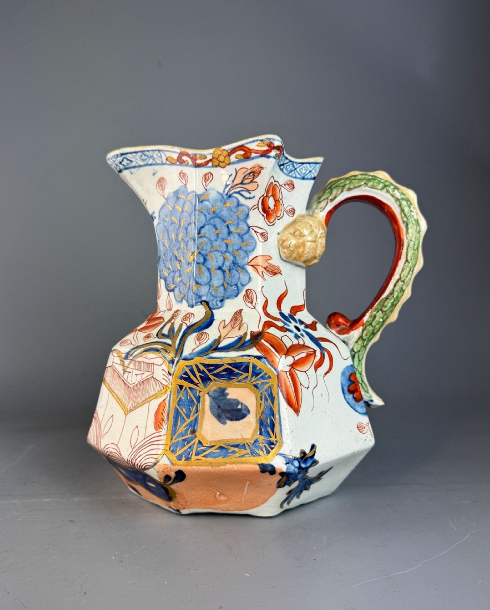 An octagonal ironstone ceramic jug decorated with hand-painted Imari style floral patterns and featuring a sculpted green dragon handle.