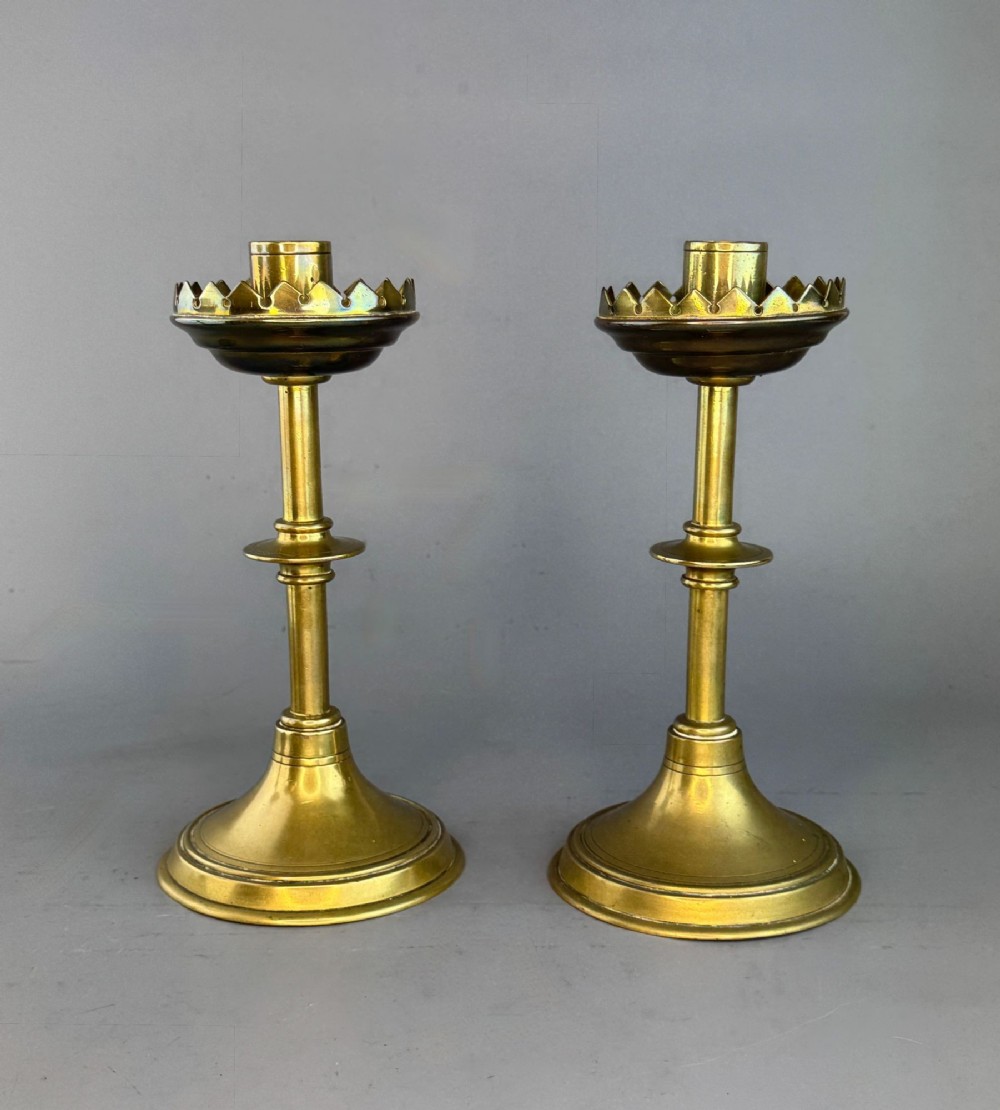 A pair of Victorian brass candlesticks featuring turned column stems, circular bases, and castellated drip pans.