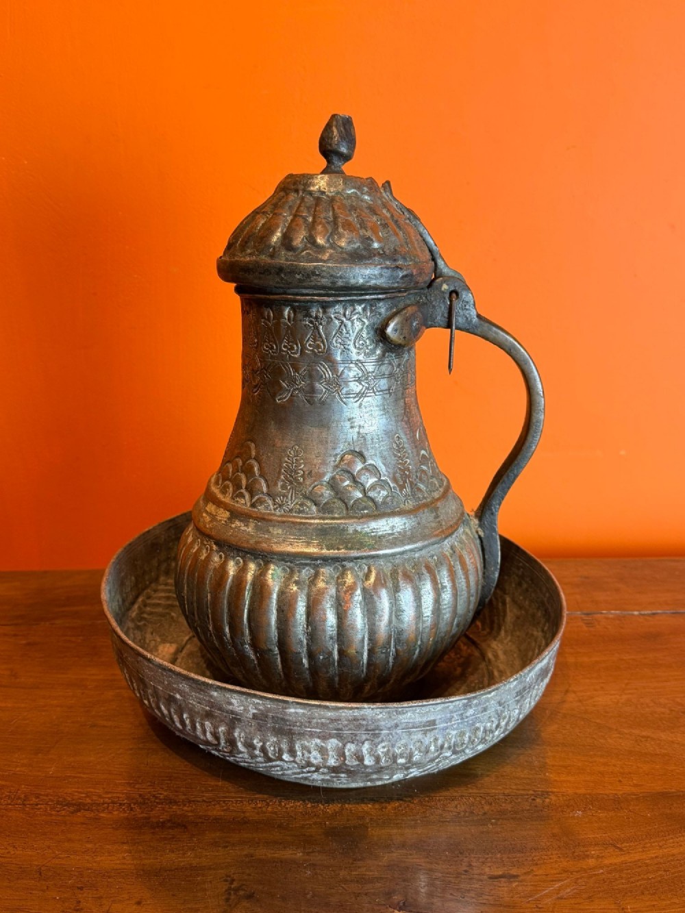 An antique Persian tinned copper ewer featuring a fluted body, hinged lid, and handle, set inside a matching circular shallow basin.
