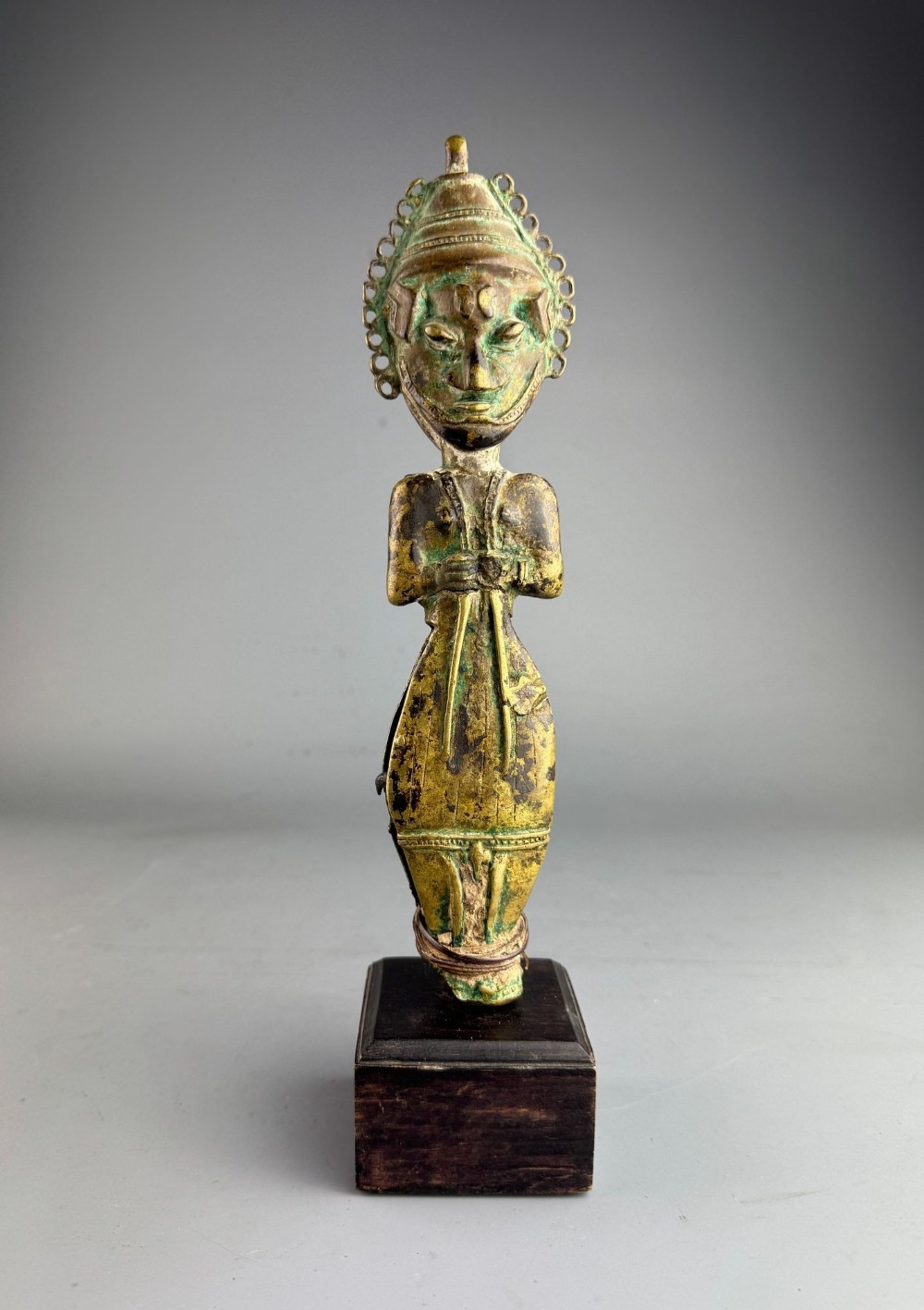 A 19th-century West African Yoruba Ogboni bronze Janus figure featuring a verdigris patina, detailed facial scarification, and a circular halo headpiece, displayed on a square wooden base.
