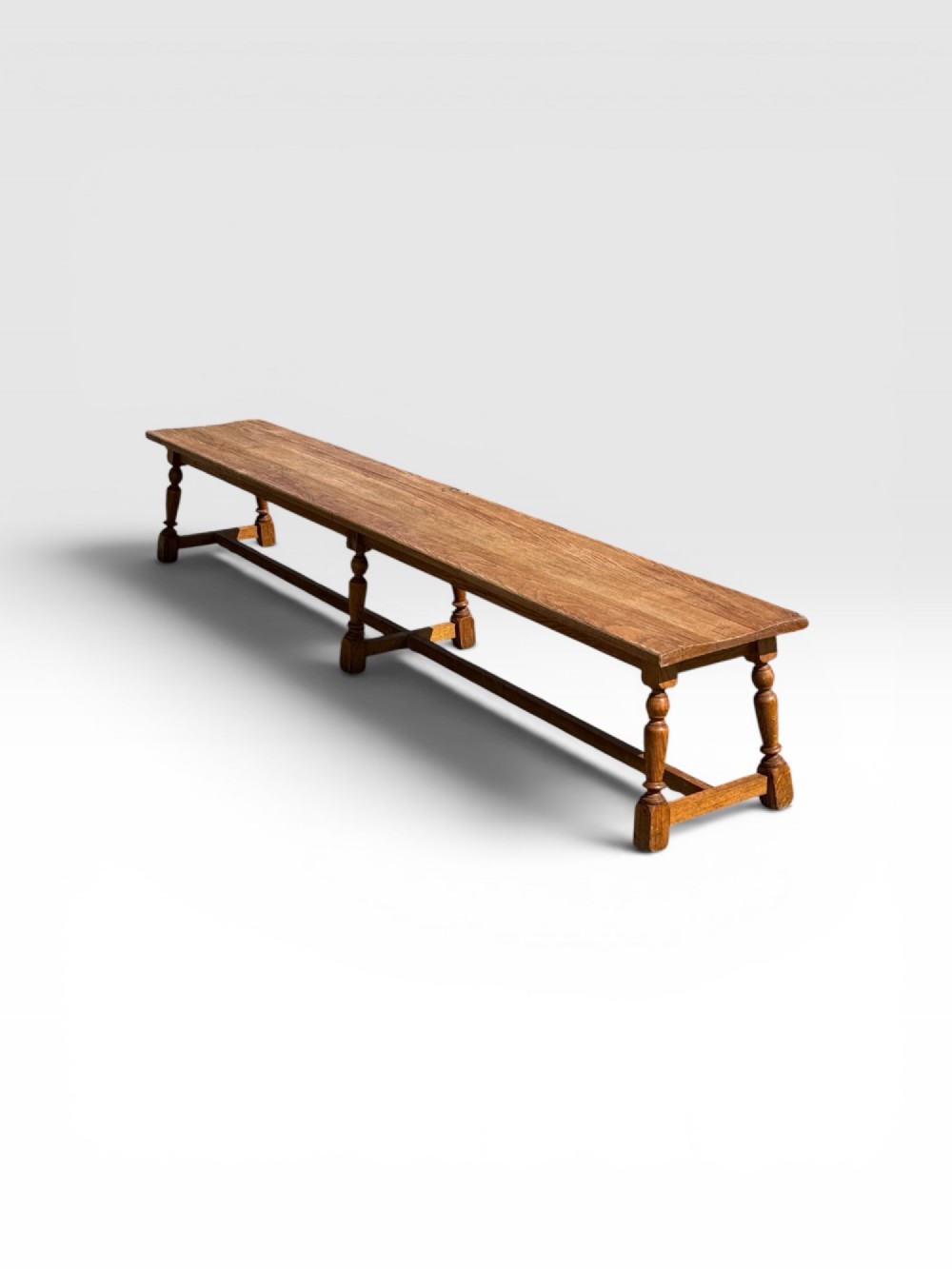 An exceptionally long rustic antique oak bench featuring a smooth rectangular seat, turned legs, and low connecting stretchers.