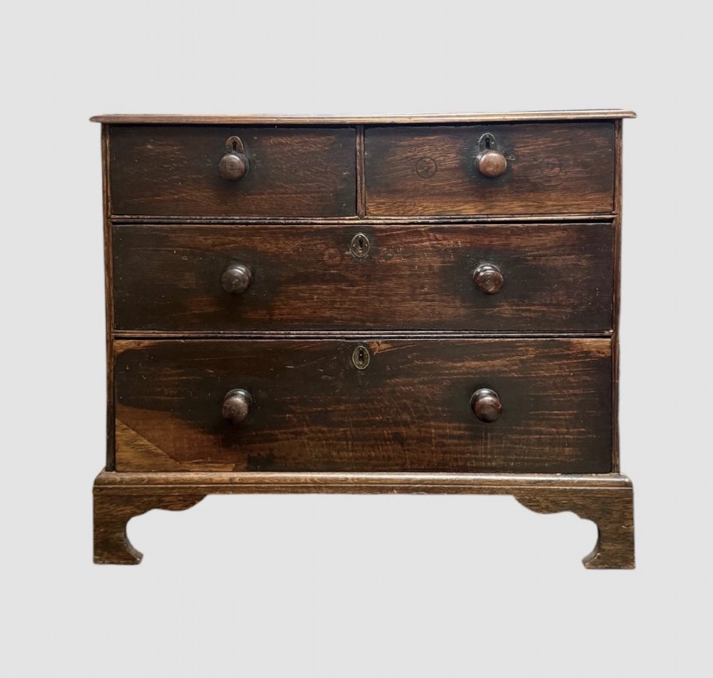 An eighteenth century dark oak chest of drawers featuring two short drawers over two long drawers with turned wooden knobs and bracket feet.