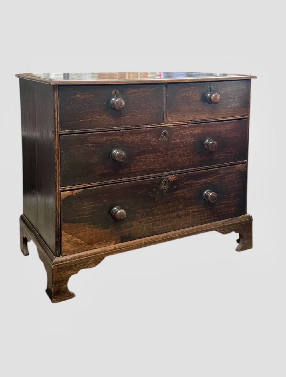 An eighteenth century dark oak chest of drawers featuring two short drawers over two long drawers with turned wooden knobs and bracket feet. View II
