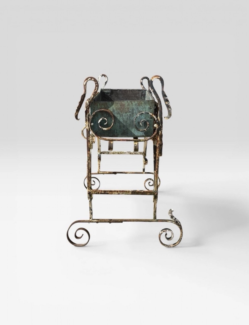 A white painted wrought iron planter stand featuring decorative scrollwork legs holding a rectangular green oxidised metal trough liner. View IV