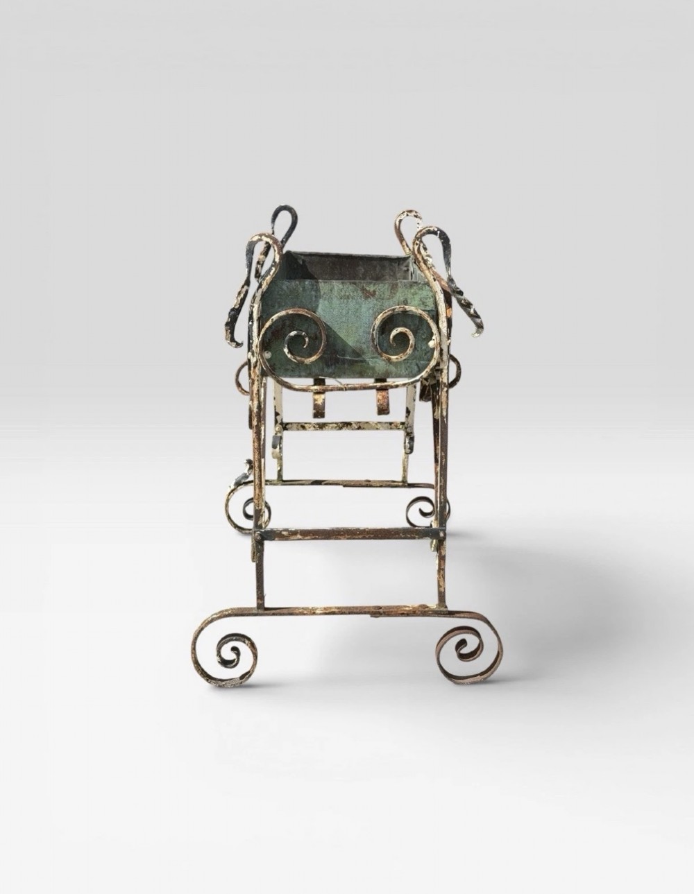 A white painted wrought iron planter stand featuring decorative scrollwork legs holding a rectangular green oxidised metal trough liner. View V