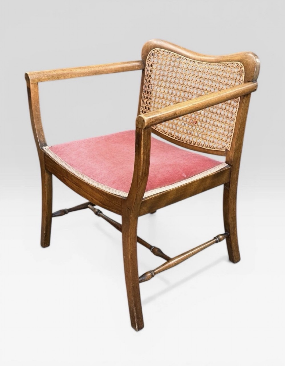 An antique childs wooden armchair featuring a cane woven backrest, swept armrests, turned stretchers, and a red velvet upholstered drop-in seat. View II
