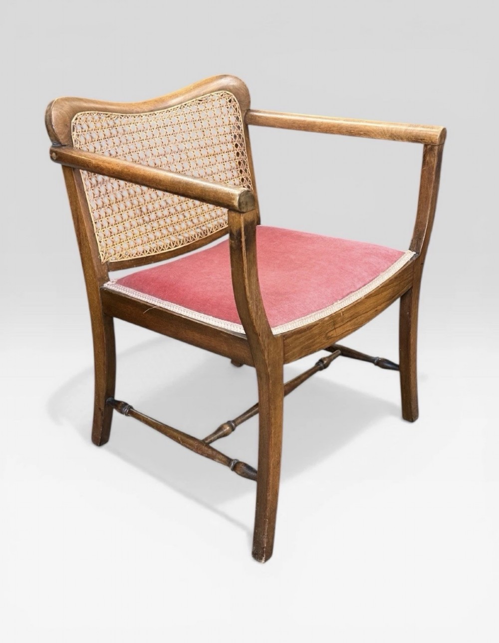 An antique childs wooden armchair featuring a cane woven backrest, swept armrests, turned stretchers, and a red velvet upholstered drop-in seat. View III