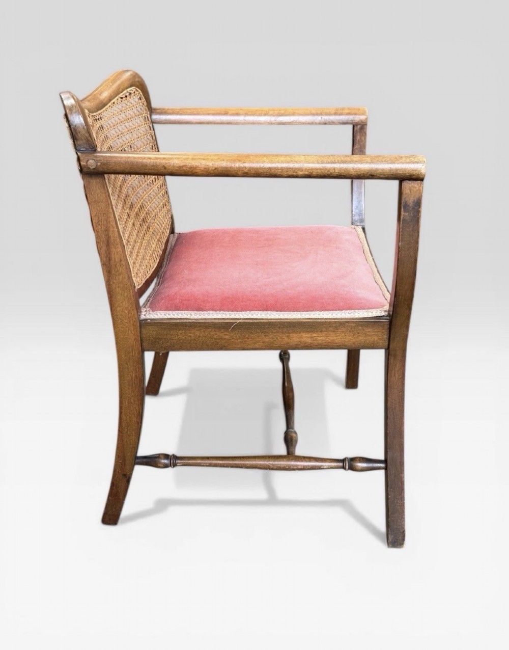 An antique childs wooden armchair featuring a cane woven backrest, swept armrests, turned stretchers, and a red velvet upholstered drop-in seat. View IV