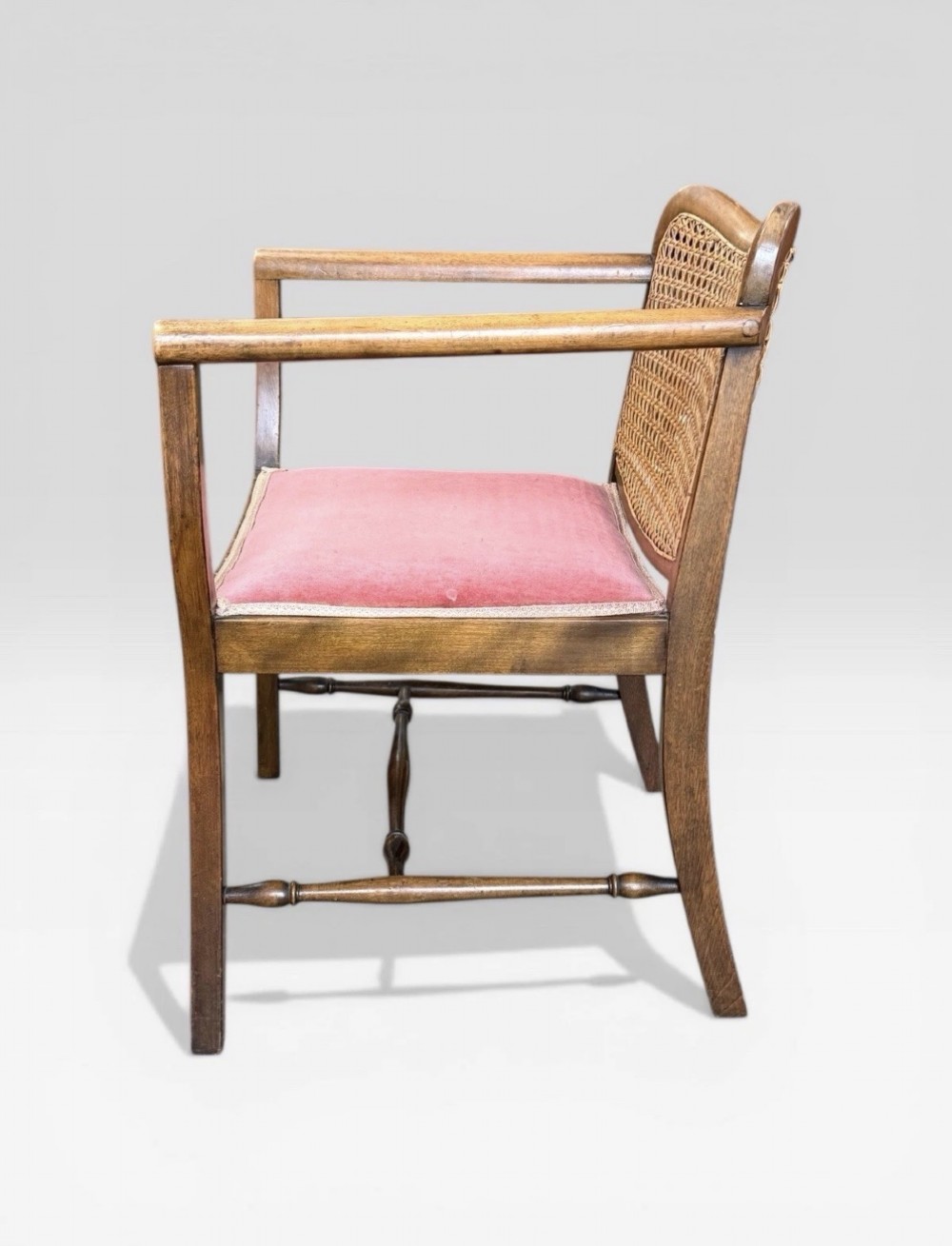 An antique childs wooden armchair featuring a cane woven backrest, swept armrests, turned stretchers, and a red velvet upholstered drop-in seat. View V