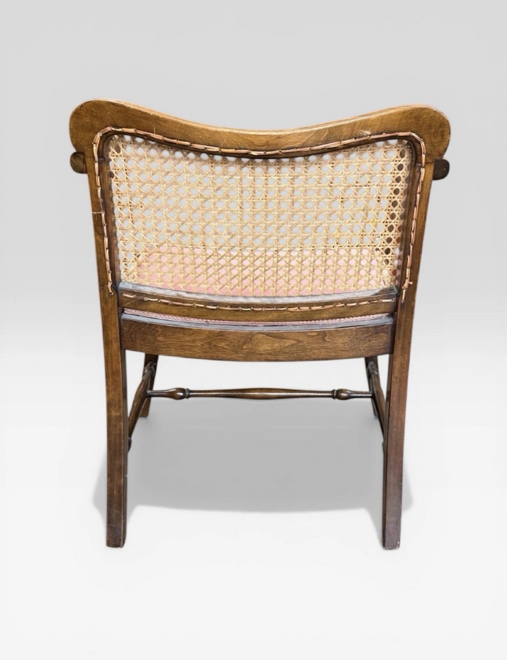 An antique childs wooden armchair featuring a cane woven backrest, swept armrests, turned stretchers, and a red velvet upholstered drop-in seat. View VI