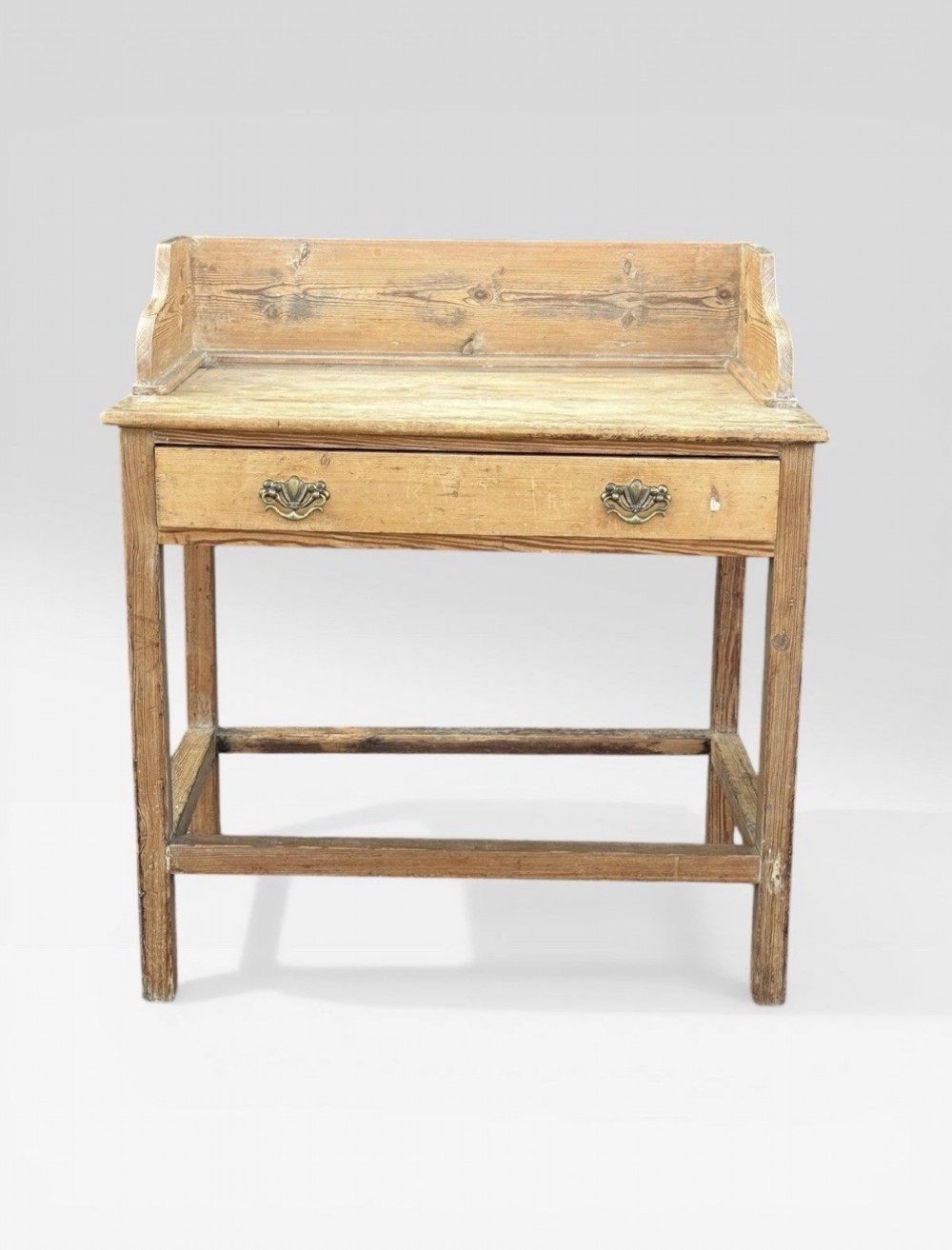 A nineteenth-century Victorian natural pine washstand featuring a raised splashback gallery, a single front drawer with brass handles, and square legs joined by a box stretcher.