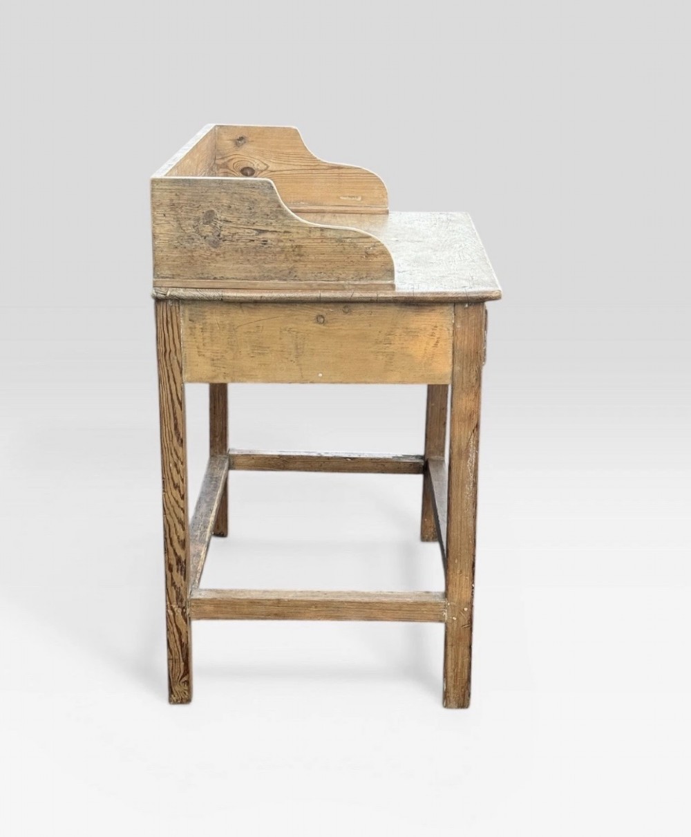 A nineteenth-century Victorian natural pine washstand featuring a raised splashback gallery, a single front drawer with brass handles, and square legs joined by a box stretcher. View IV