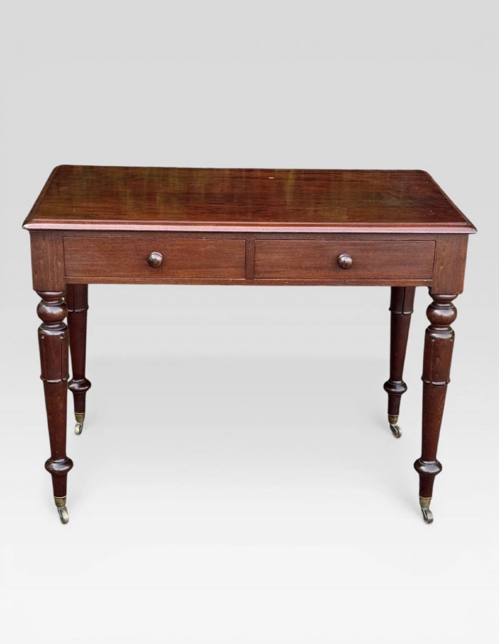 A Victorian dark mahogany side table featuring two drawers with circular wooden knobs, standing on four turned legs equipped with brass castors.