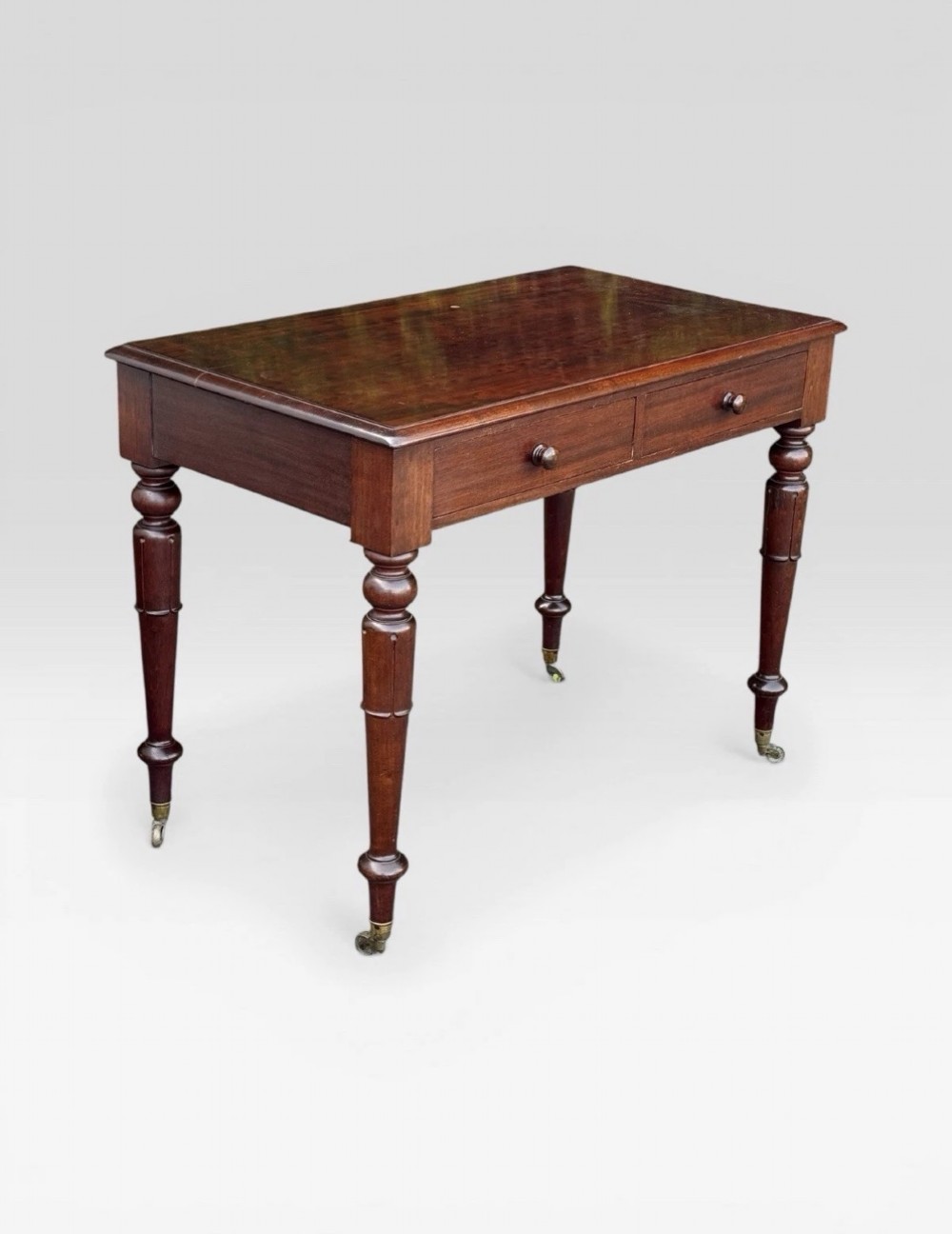 A Victorian dark mahogany side table featuring two drawers with circular wooden knobs, standing on four turned legs equipped with brass castors. View II