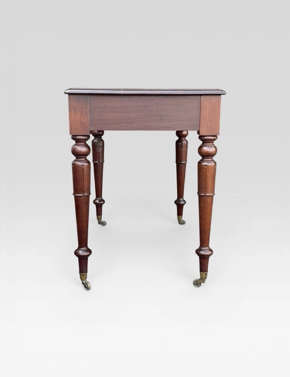 A Victorian dark mahogany side table featuring two drawers with circular wooden knobs, standing on four turned legs equipped with brass castors. View III