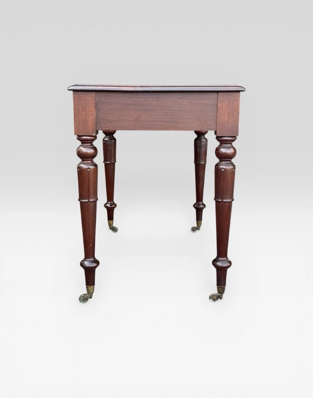 A Victorian dark mahogany side table featuring two drawers with circular wooden knobs, standing on four turned legs equipped with brass castors. View IV